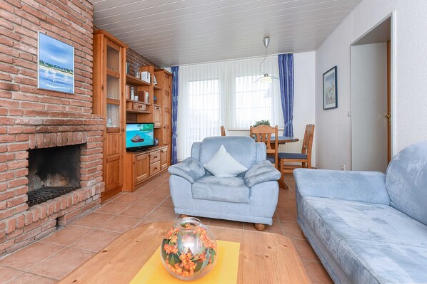 A living room with a brick fireplace, a blue armchair, a sofa, a wooden cabinet with books, and a television.
