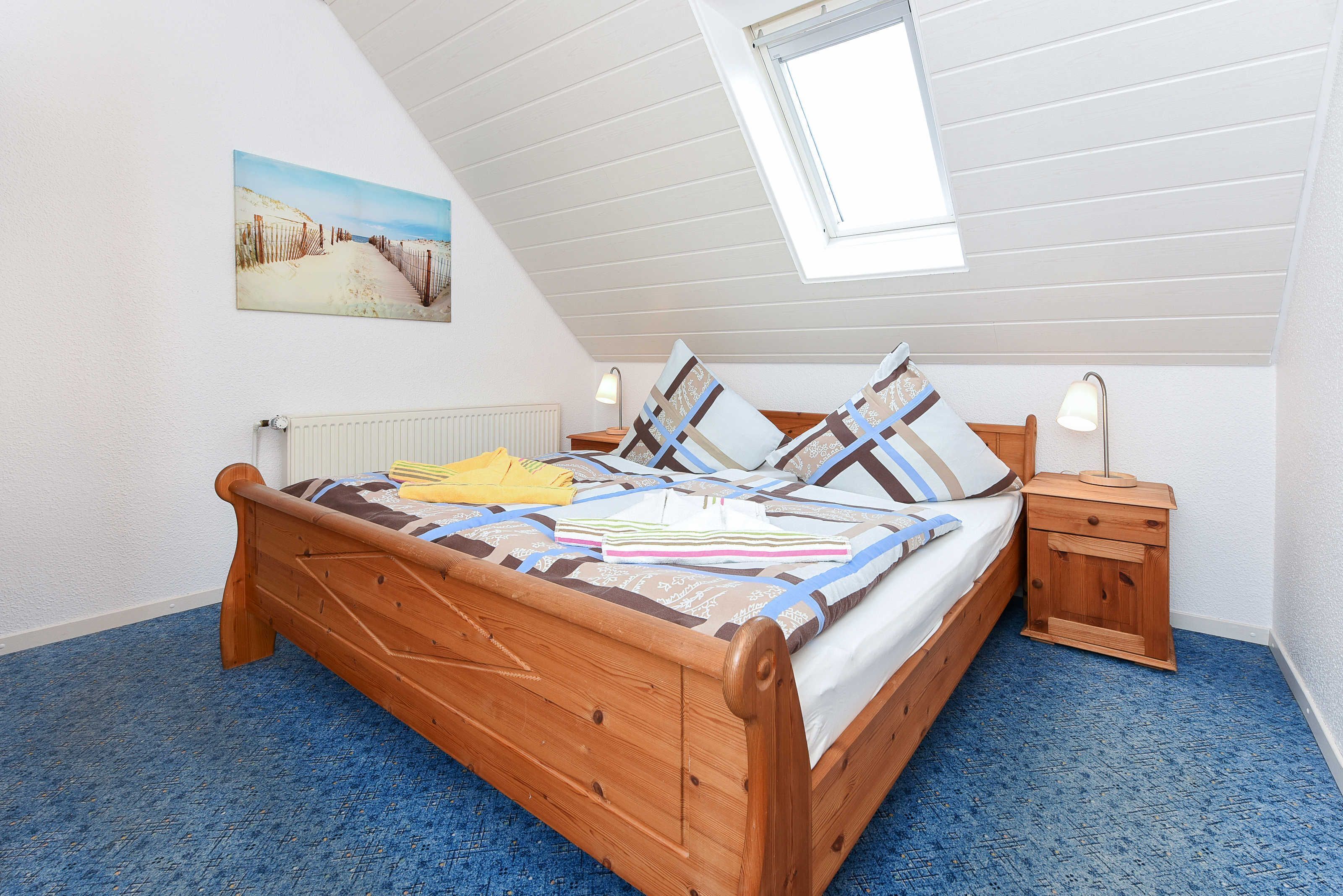 Ein Schlafzimmer mit Schräge, einem hölzernen Bett, einem Nachttisch und einem Bild an der Wand.