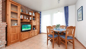 Et spiseområde med et træbord og stole, et fjernsyn på et skab, og en murstensvæg.