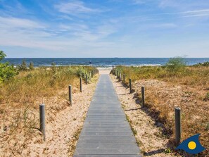 A wooden boardwalk leading to the beach, flanked by sand and vegetation. - Wool Strandperle, white 25 - VS 25 (Heringsdorf)