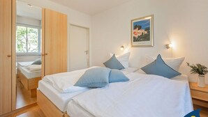 Une chambre avec deux lits, une armoire en bois, une fenêtre donnant sur des arbres et un tableau encadré au mur.