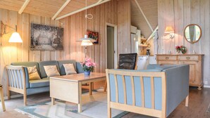 En mysig stuga med en soffa, ett litet bord och en stol. På väggen hänger en tavla, och det finns även en lampa och en spegel.