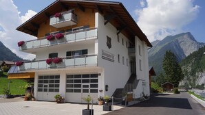 Un edificio de dos pisos con balcones, un garaje y montañas al fondo.