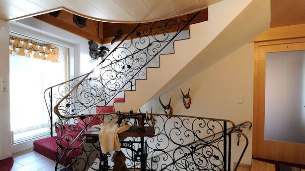 Una escalera con barandillas de metal ornamentadas, un banco acolchado rojo y adornos de cornamenta en la pared.