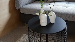 Una sala moderna con un sofá gris, cojines estampados, una mesa redonda negra con dos jarrones blancos y una pared de madera.