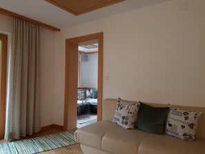 A living room with a beige sofa, patterned cushions, a striped rug, and a wooden-framed doorway leading to another room. - Apartment 2 - Rüf Marlene (Au)