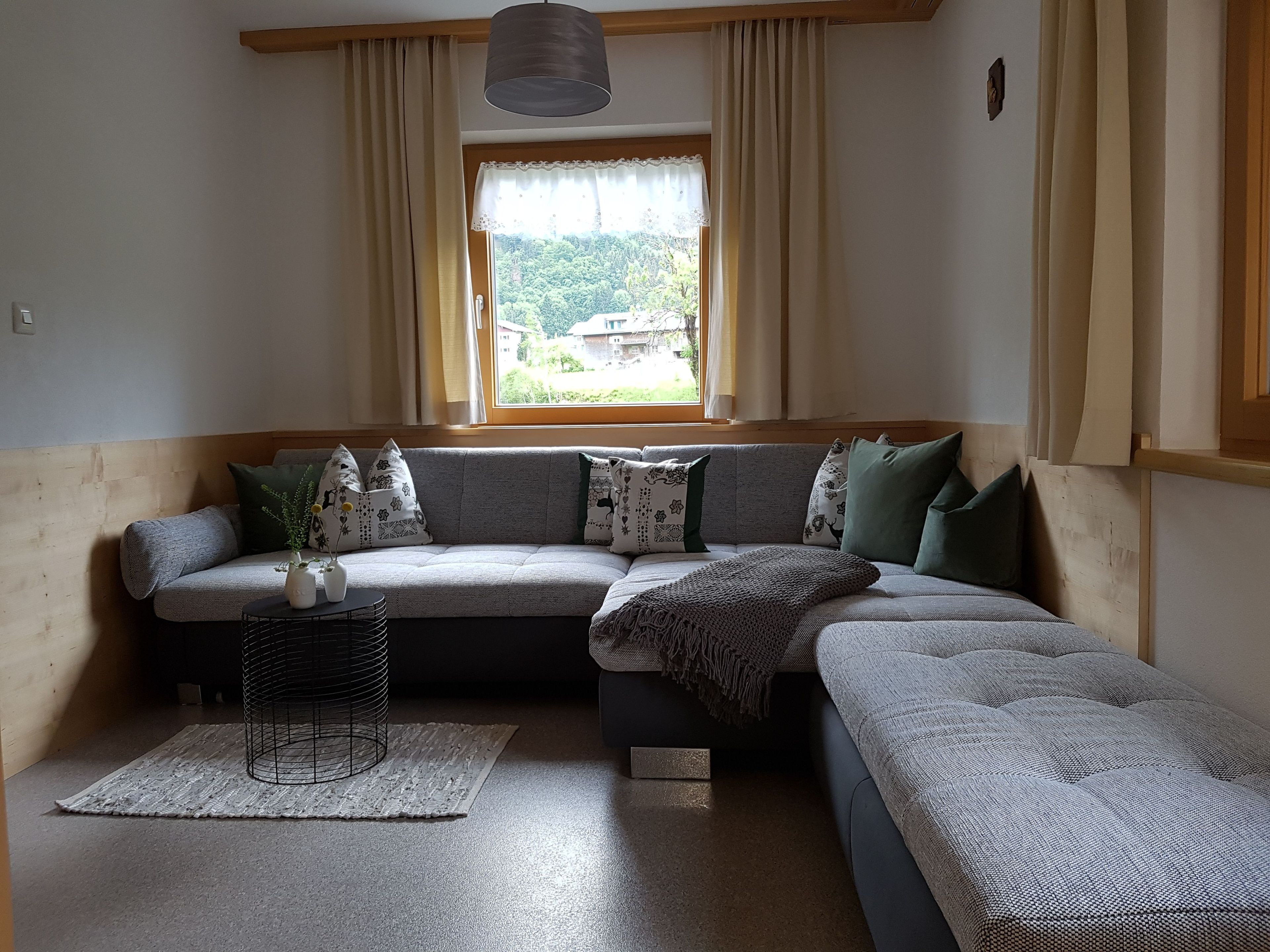A cozy living room with a sectional sofa, a small side table, and a window with curtains.