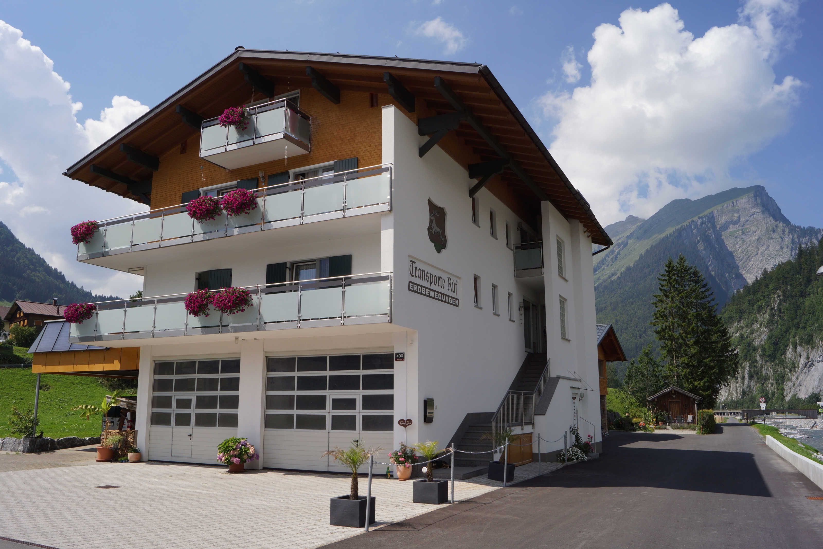 A two-story building with balconies, a garage, and a mountain backdrop.