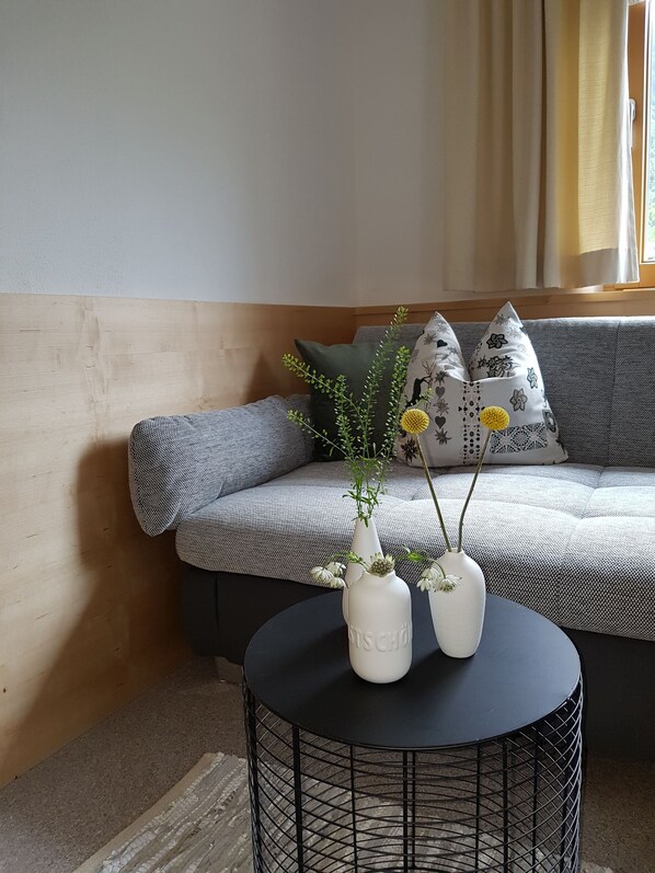 A modern living room with a grey sofa, patterned cushions, a black round table with two white vases, and a wooden wall.