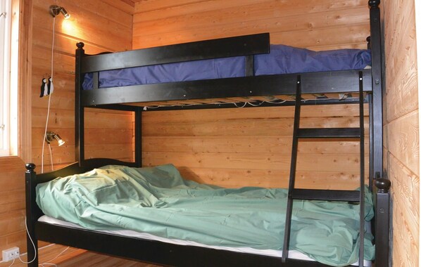 A bunk bed with a ladder, a window with a light fixture, and a power outlet on the floor.