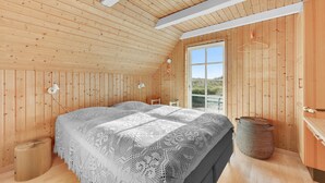 A cozy room with wooden walls and ceiling, a large bed with a patterned blanket, a small stool, and a woven basket. - Beautiful home in Ringkøbing with WiFi (Ringkøbing)