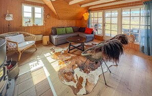 A cozy cabin interior with wooden walls, a sofa, a dining table, a chair, and a large fur rug.