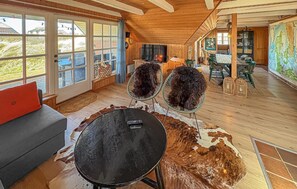 A spacious room with a large window, a wooden ceiling, a round table, and a cowhide rug.