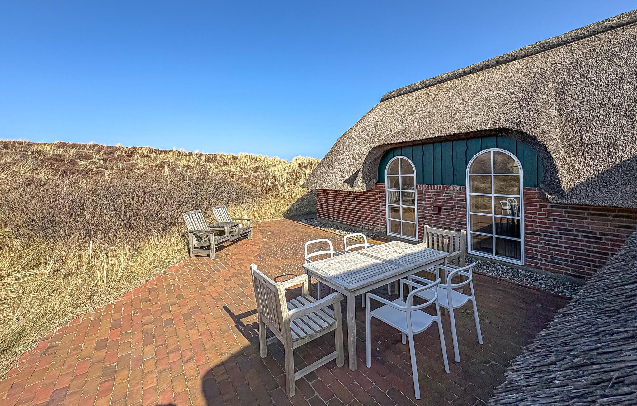 A thatched-roof building with a brick patio, outdoor seating, and a view of a field.