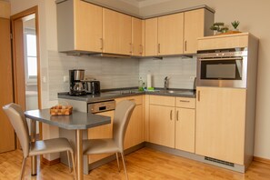 Une cuisine moderne avec des meubles en bois, un four encastré, une machine à café et un coin repas avec deux chaises.