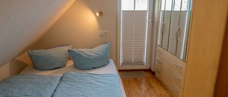 A bedroom with a bed, pillows, a dresser, and a window with blinds.