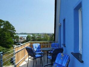 Un balcon avec des chaises bleues et une table, d’où l’on peut admirer un plan d’eau et des bâtiments.