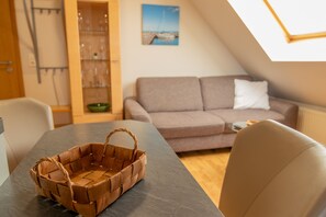 A cozy room with a dining table, a wicker basket, a sofa, and a view of the outdoors through a skylight. - Vacation apartment 3 - Holiday apartments in Blu Hus (Kröslin)