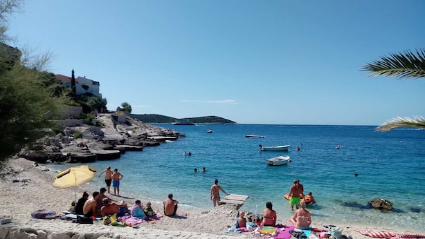 Une plage avec une eau d’un bleu limpide, un rivage rocheux et des gens qui prennent un bain de soleil.