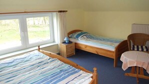 Une chambre avec deux lits simples, une chaise en bois, une petite table et une fenêtre avec des rideaux.