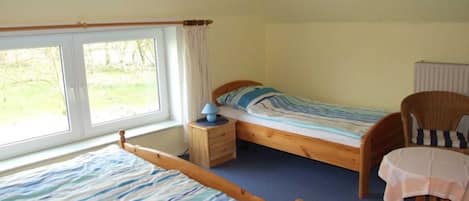A bedroom with two single beds, a wooden chair, a small table, and a window with curtains.