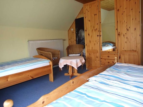 A bedroom with two single beds, a chair, a small table, and wooden wardrobes.
