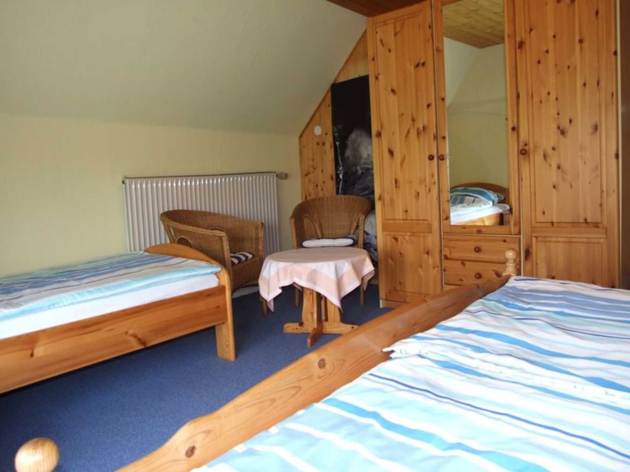 Une chambre avec deux lits simples, une chaise, une petite table et des armoires en bois.