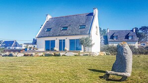Una casa moderna con techo inclinado, amplios ventanales y un monumento de piedra al frente.