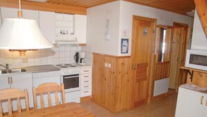 A compact kitchen with a stove, oven, and sink, wooden cabinets, and a dining table with chairs.