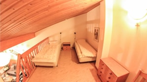 A small attic bedroom with two single beds, a wooden ceiling, and a wooden bench.