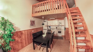 A compact kitchen with white cabinets, a black dining table with chairs, and a wooden staircase leading to an upper level.