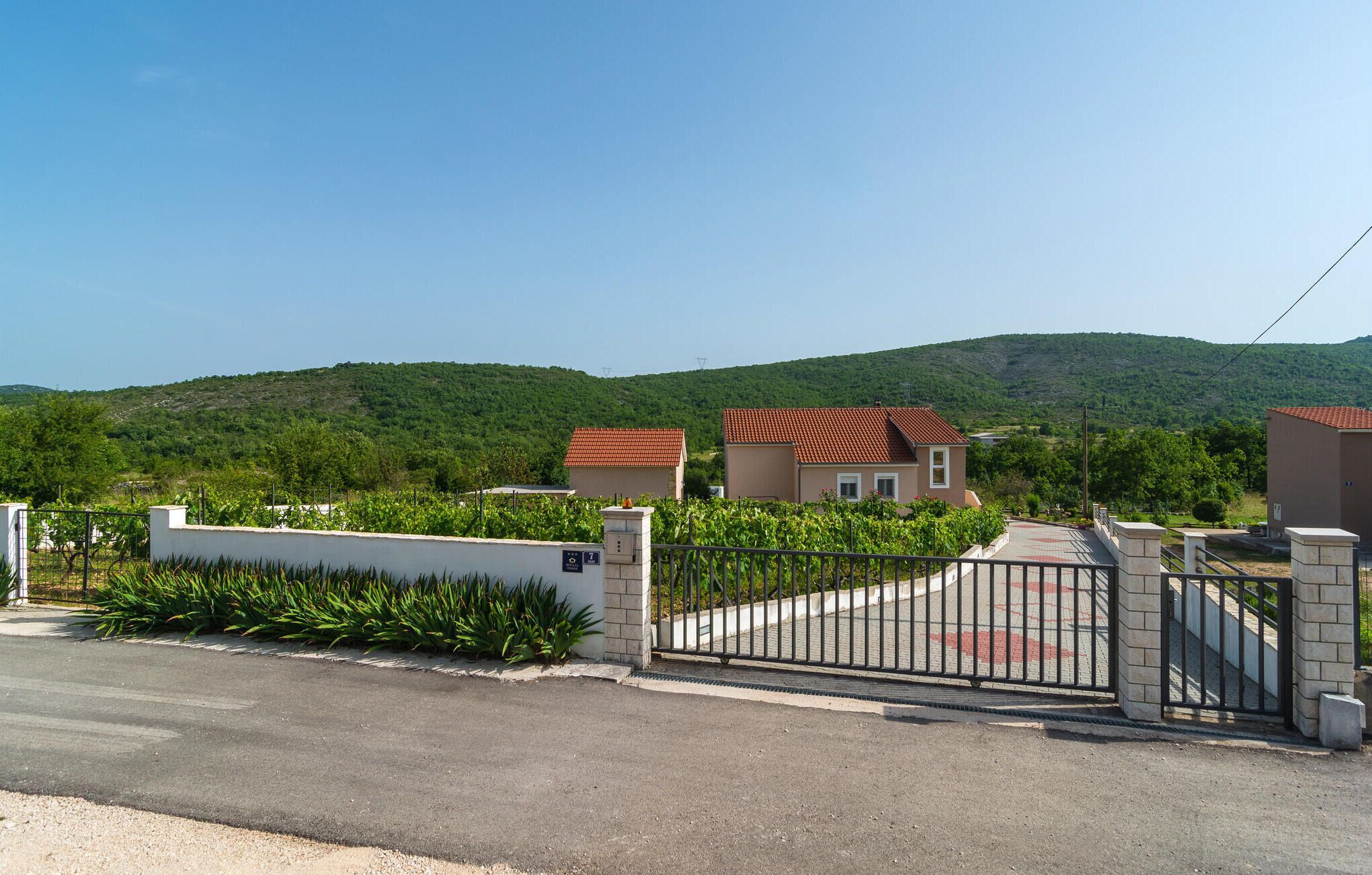 Un lotissement résidentiel fermé, avec des maisons, une route asphaltée et un paysage vallonné en arrière-plan.
