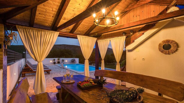 An outdoor pool area with wooden benches and a table with fruits and a vase.