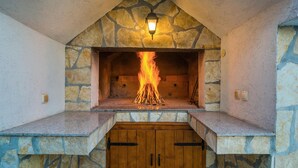 A stone fireplace with a fire burning inside, a wooden door below, and a stone wall with a stone pattern.