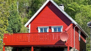 A red wooden house with a stone foundation, a balcony, and a chimney.