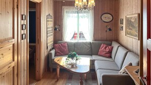 A cozy cabin interior with a wooden interior, a sofa with cushions, a small table with a plant, and a chandelier.
