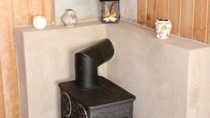 A corner room with a black wood-burning stove, a small lantern, and a wall-mounted candle holder.