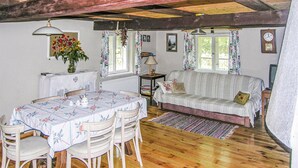 Una habitación acogedora con techo de madera, un sofá, una mesa con sillas y un ventanal con cortinas.