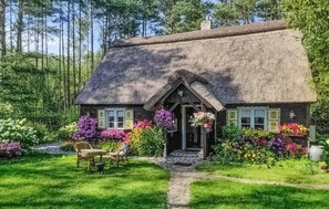 Een rieten huisje met een pad van stenen dat naar de ingang leidt, omgeven door weelderige begroeiing en kleurrijke bloemen.