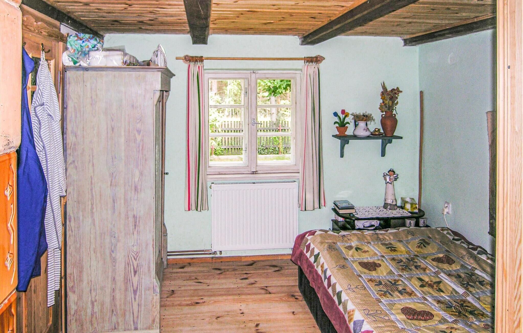 Une chambre confortable avec un plancher en bois, un lit recouvert d’une courtepointe à motifs, un radiateur, une fenêtre avec des rideaux et une étagère ornée d’objets décoratifs.