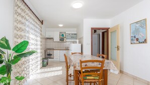 A dining area with a table and chairs, a kitchen in the background, and a door leading to another room.