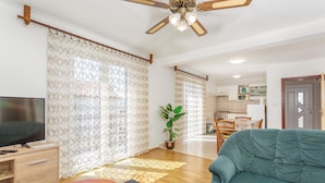 A living room with a TV, sofa, curtains, and a ceiling fan.