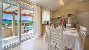 Zona pranzo con tavolo apparecchiato per quattro, cucina dotata di elettrodomestici moderni e vista su piscina e paesaggio attraverso ampie porte scorrevoli in vetro.