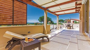 Un'area salotto esterna coperta con tavolo e sedie, un pannello di legno a listelli e vista sul paesaggio.
