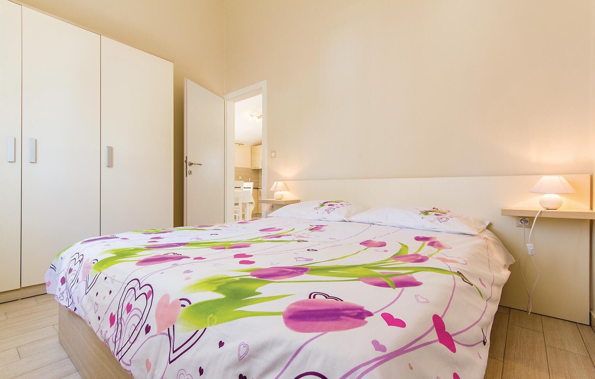A bedroom with a bed, bedside lamps, a wardrobe, and a door leading to another room.