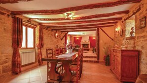 Une salle à manger rustique avec des poutres apparentes, une cheminée et une table à manger dressée pour quatre personnes.