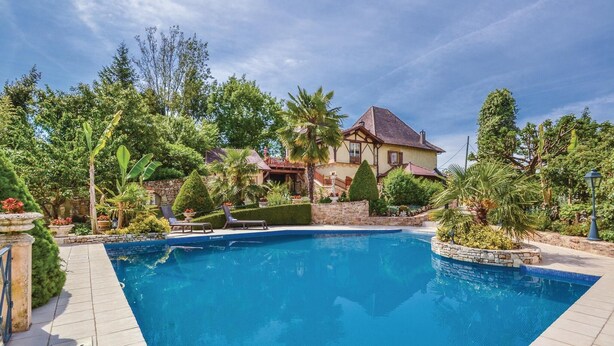 Une piscine bordée de pierres, entourée d’une végétation luxuriante et avec une grande maison en arrière-plan.