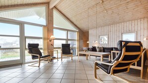 A spacious room with large windows, wooden walls, and modern furniture including leather chairs and a wooden table. - 3 bedroom lovely home in Rømø (Rømø)