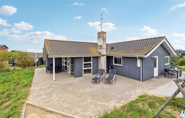 Een tweelaags huis met een pannendak, schoorsteen en een schotelantenne. Er is een overdekte patio met buitenmeubilair.