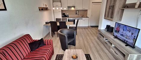 Un espacio habitable compacto con kitchenette, comedor y zona de estar con sofá y mesa de centro.